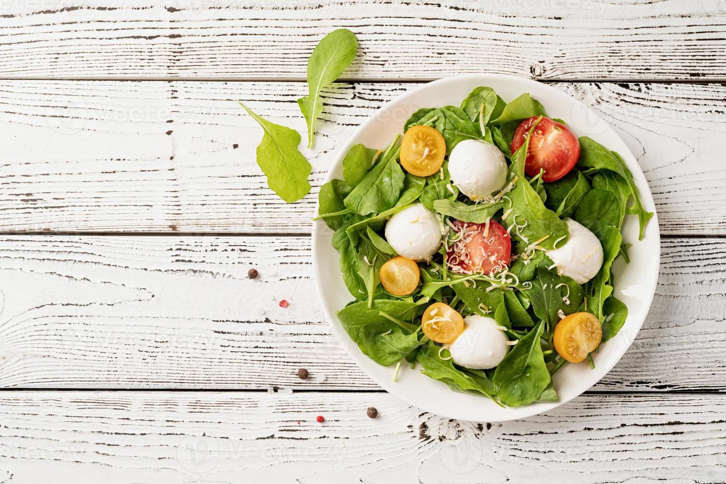 ensalada fresca con rúcula, tomates cherry, queso mozzarella y queso duro sobre fondo blanco de madera. vista superior foto