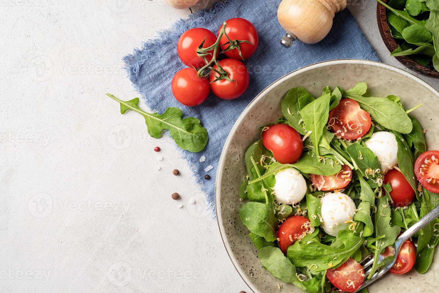 Fresh salad with arugula, cherry tomatoes, mozzarella cheese and hard cheese on white wooden background. Top view photo