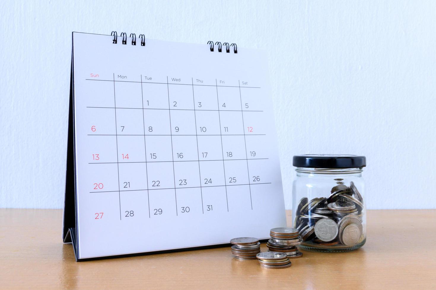 calendario con días y moneda en el frasco en la mesa de madera foto