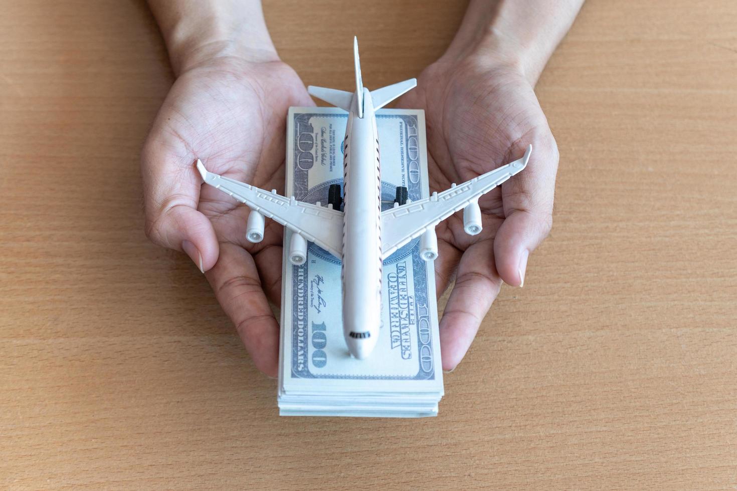 manos de hombre sosteniendo billetes de 100 dólares y avión en mesa de madera. concepto de viaje foto