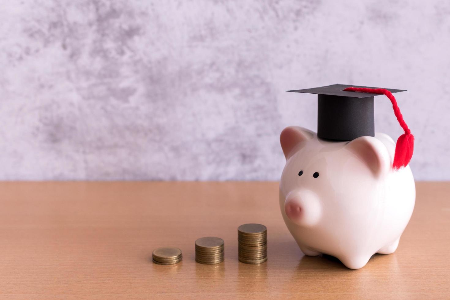 Graduation hat on piggy bank with stack of coins money on table, saving money for education concept photo