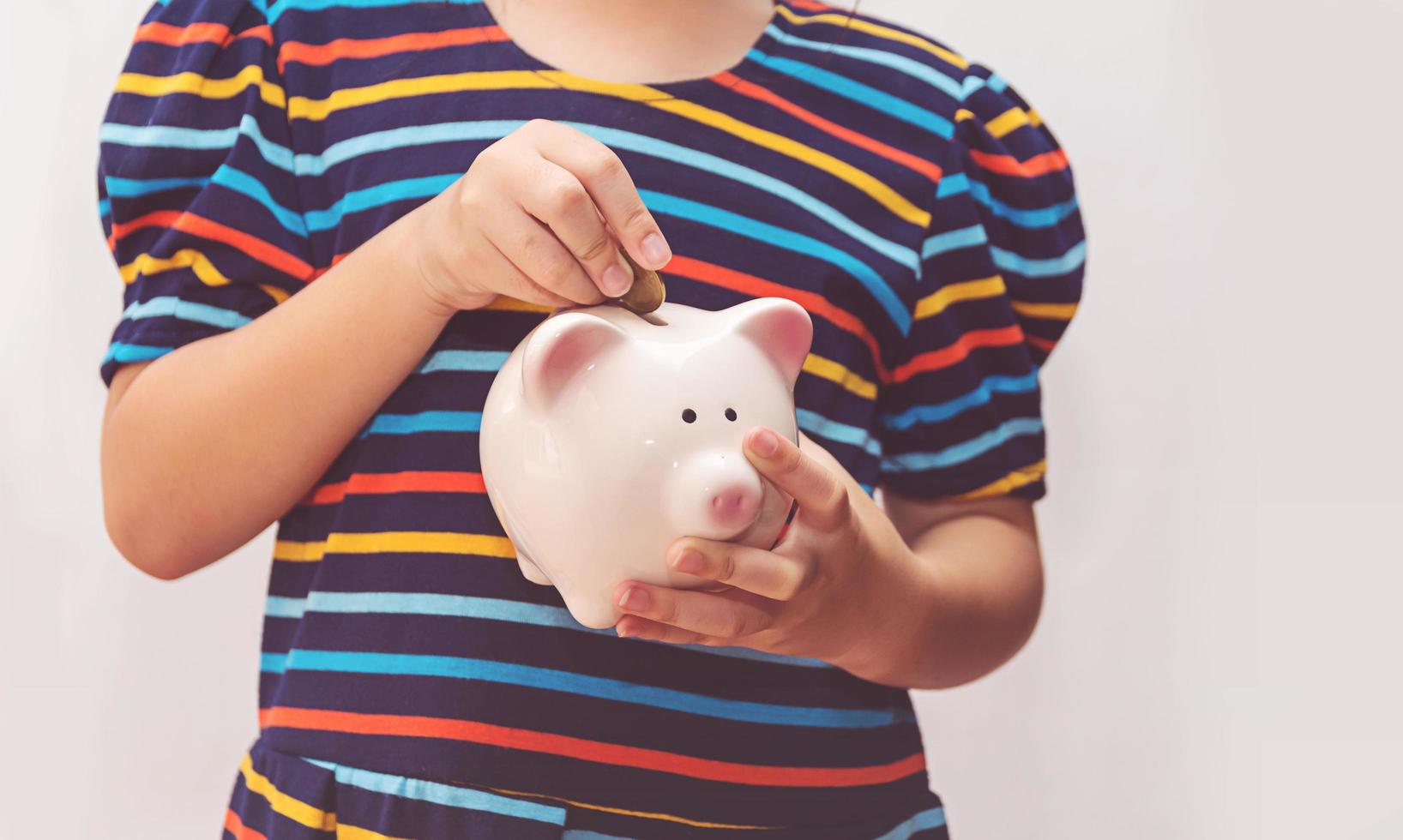 Cute little girl putting coin into piggy bank photo