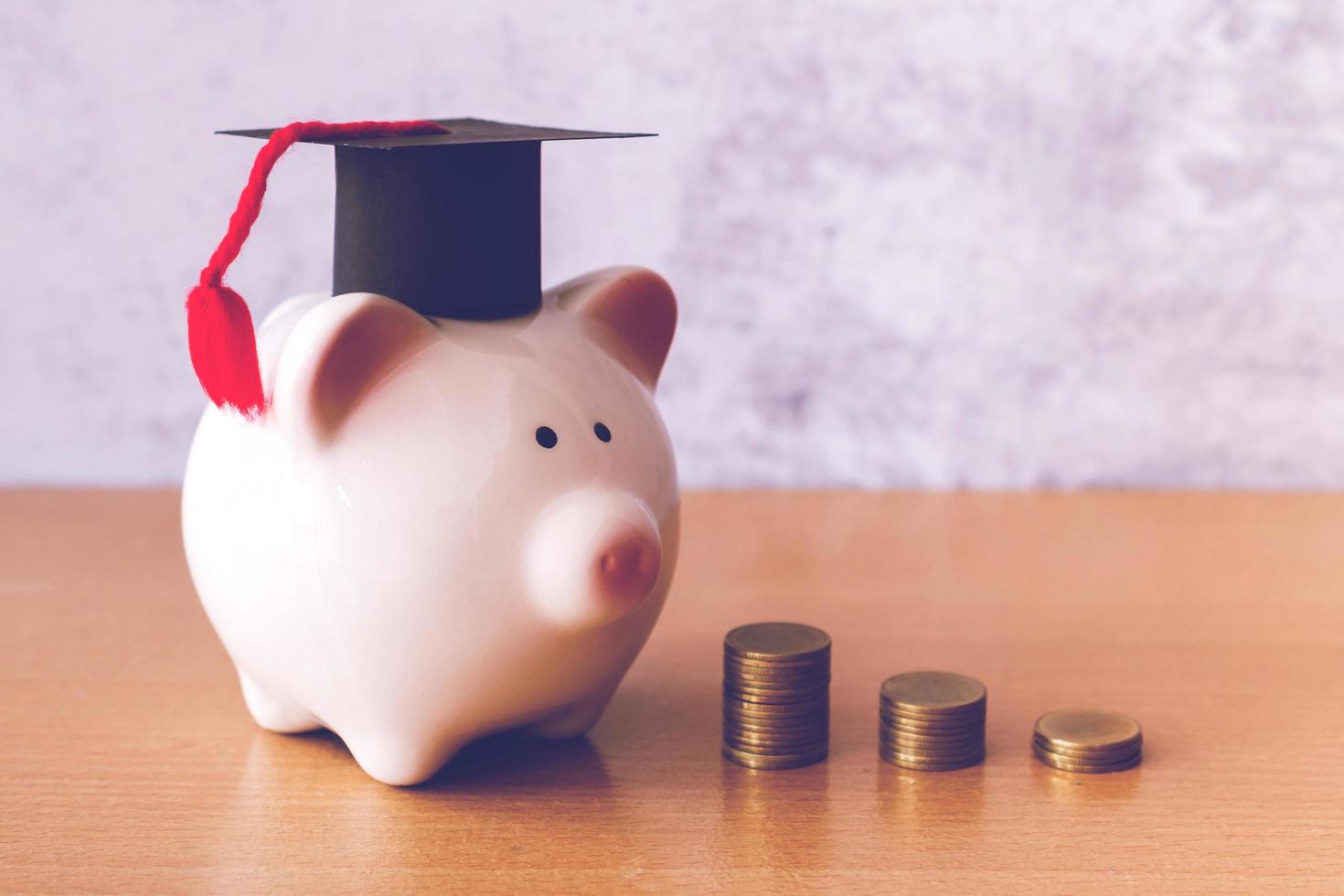 Graduation hat on piggy bank with stack of coins money on table, saving money for education concept photo