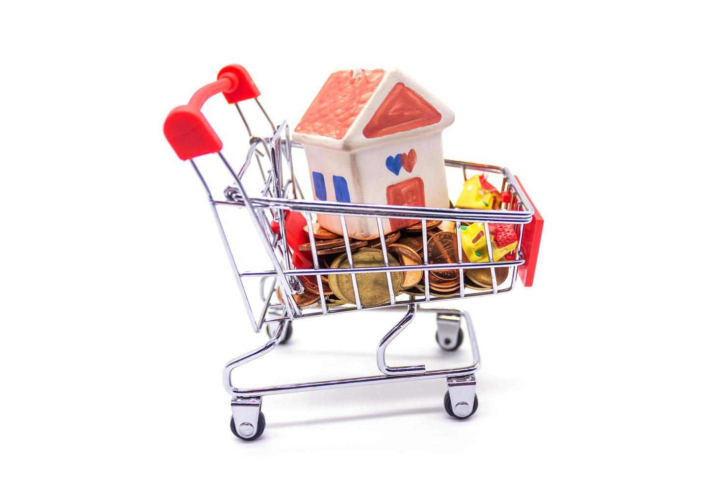 House model in mini shopping cart with stack of coins money on white blackground photo