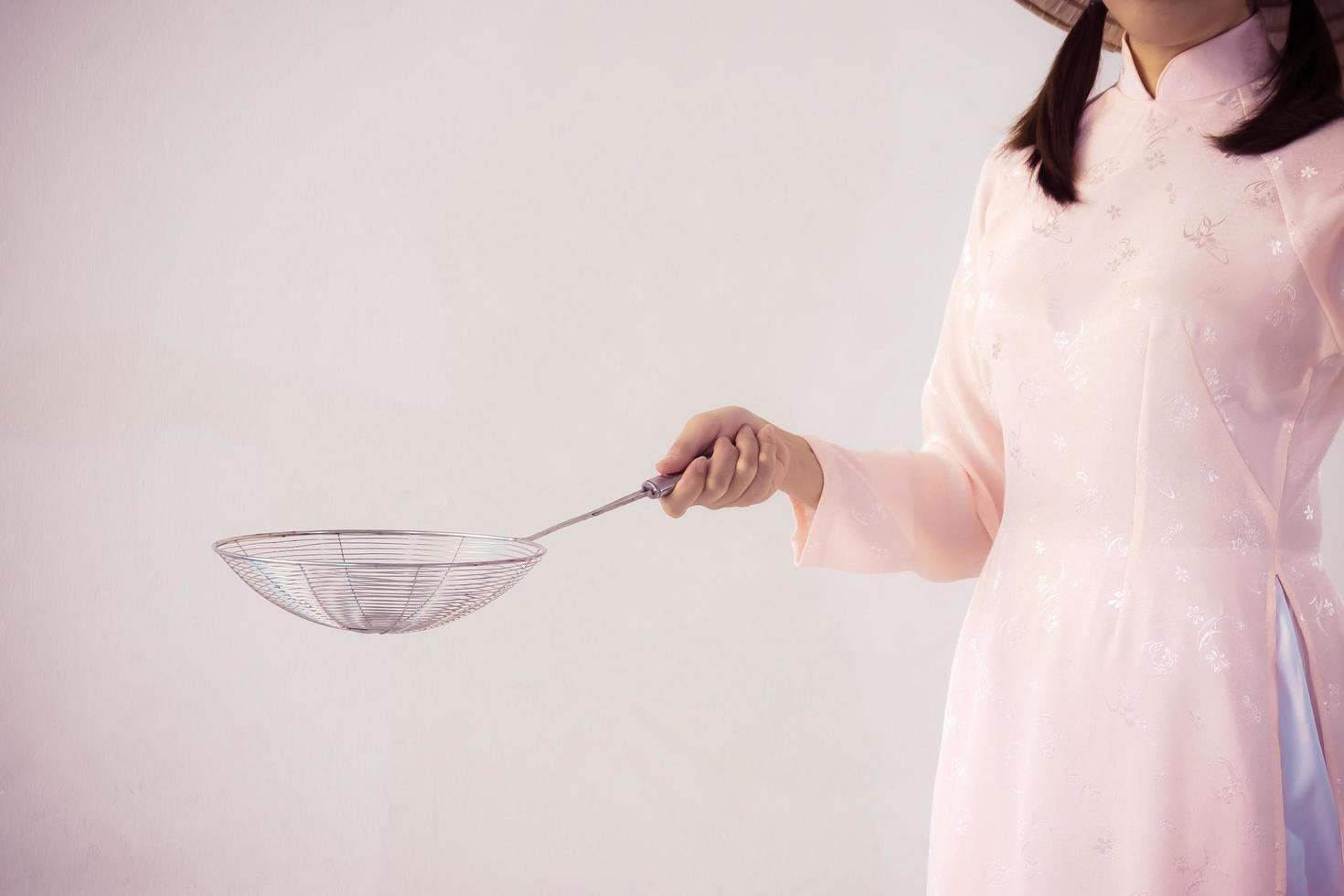 hermosa mujer con vestido rosa y sombrero de vietnam con utensilios de cocina. foto