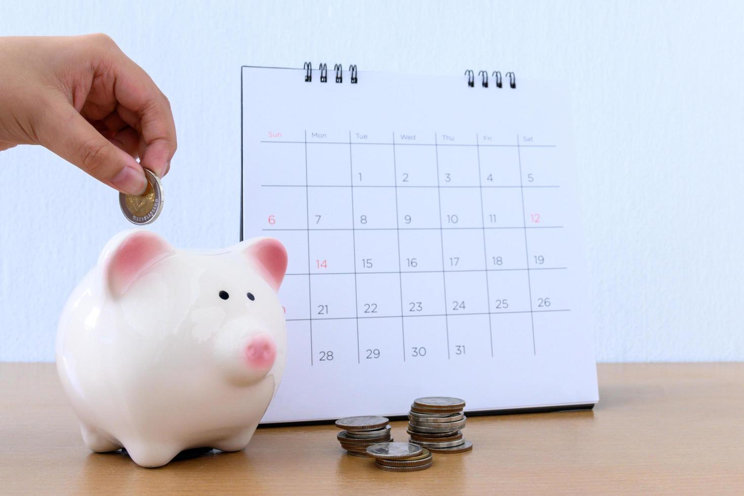 calendar and Child hand putting coin money in piggybank photo