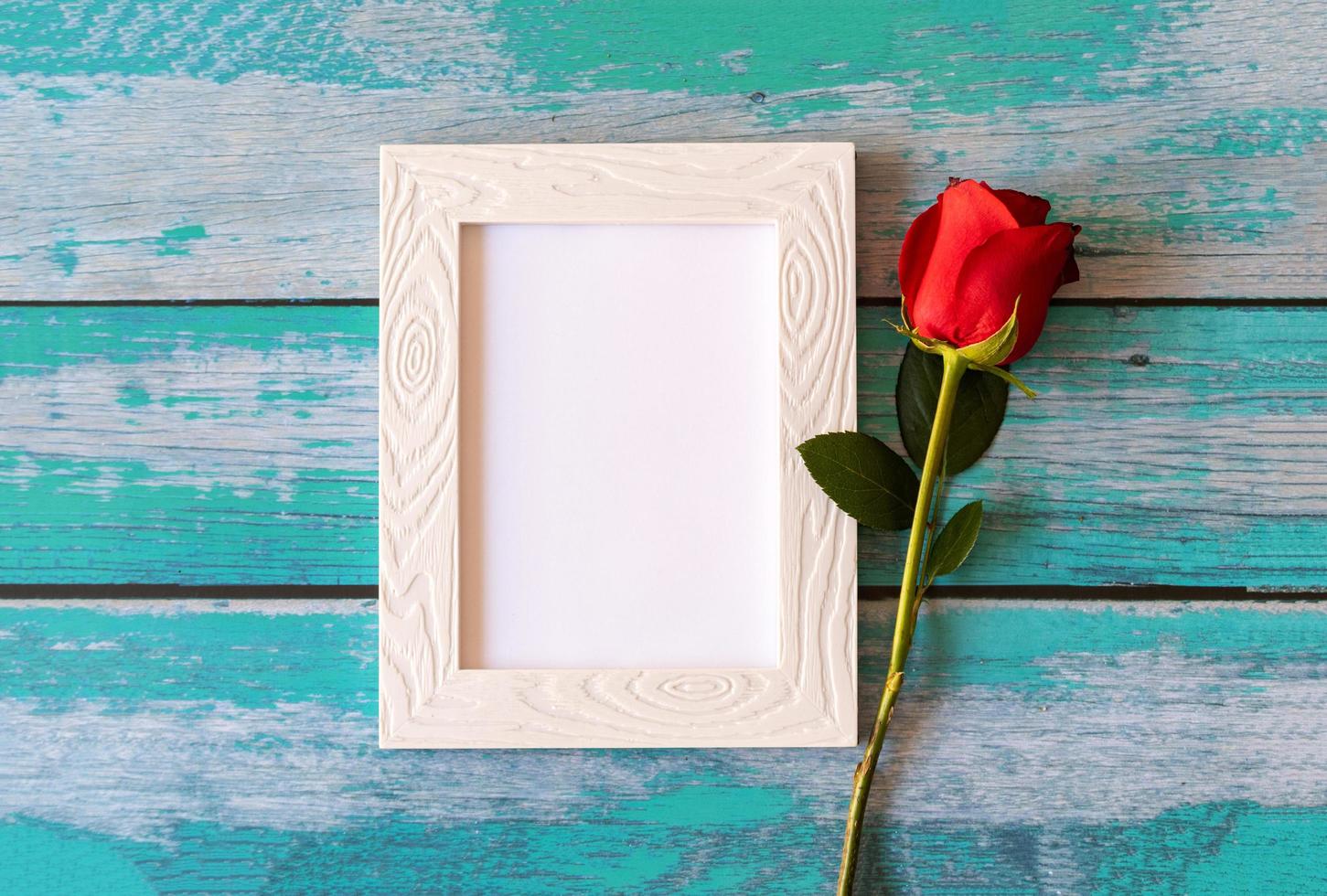 Blank photo frame and red roses over wooden table