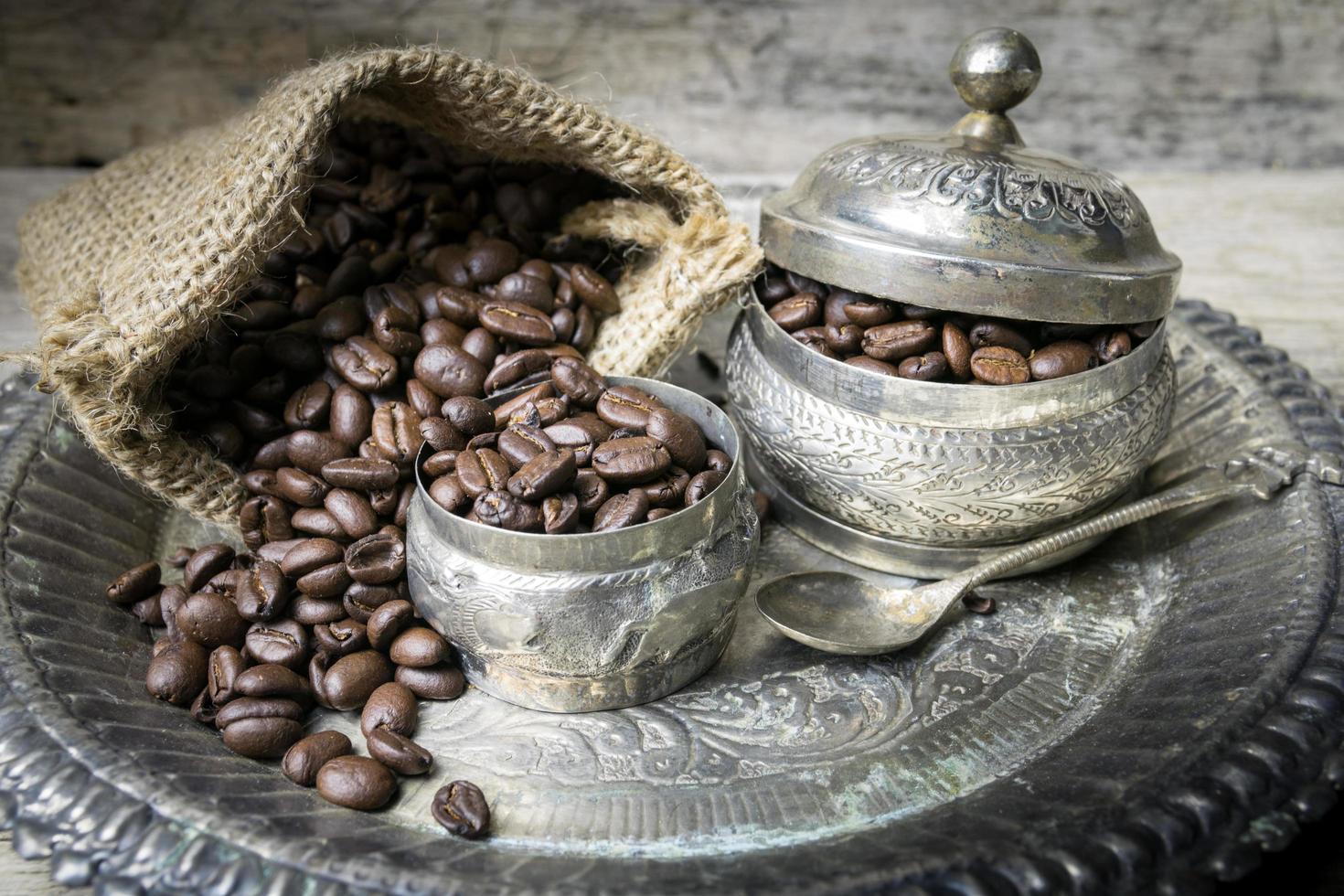 taza de plata y granos de café en bolsa de tela de saco sobre fondo de madera foto