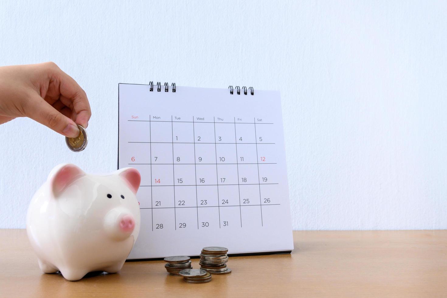 calendario y mano de niño poniendo dinero de moneda en la alcancía foto