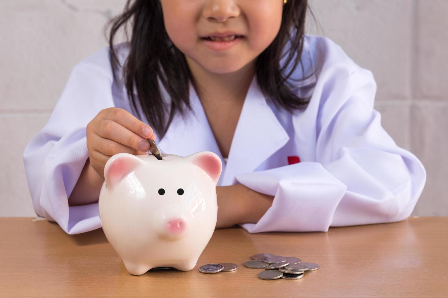 Asian girl playing as a doctor balance money in Piggy Bank photo