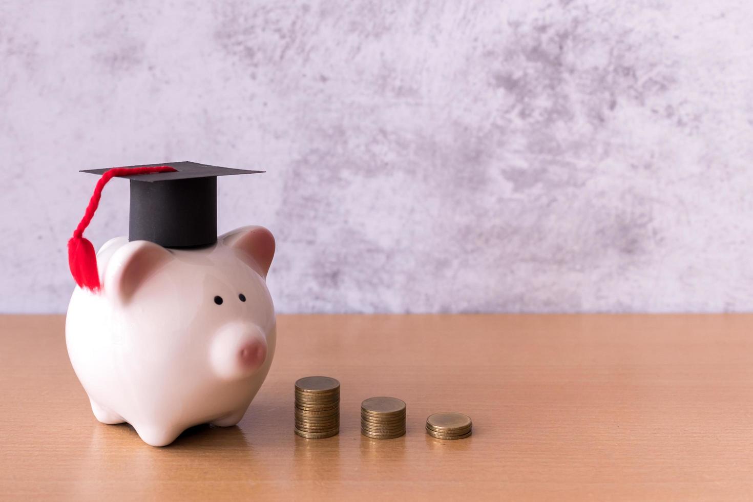 Graduation hat on piggy bank with stack of coins money on table, saving money for education concept photo