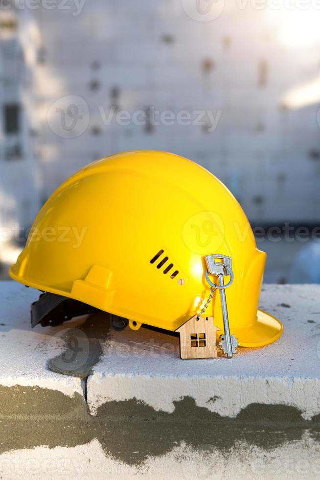 Construction yellow hardhat and key to house on window of housing made of blocks of porous concrete. Turnkey construction, future home, engineering, building. Work safety. Copy space photo