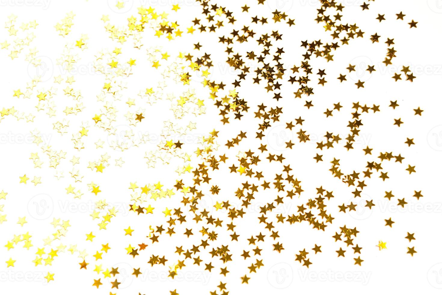 Gold sequins in the shape of stars shimmer on a white background. Backgrounds with copyspace for a holiday, party decoration, Christmas and new year, birthday and anniversary. Gradient and texture photo