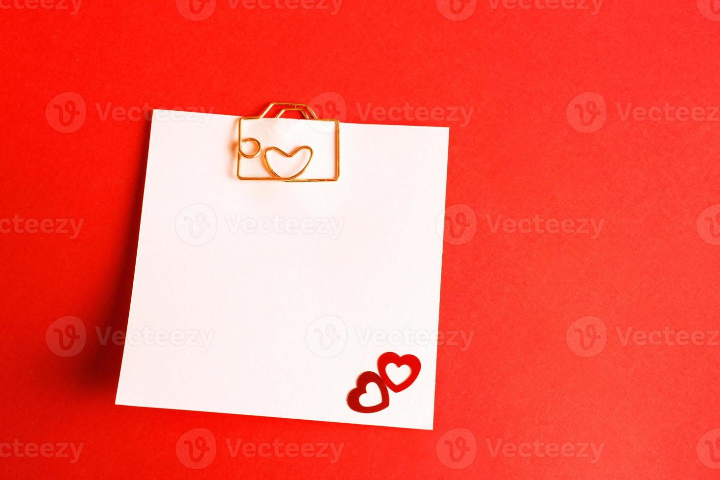 Square sheet for notes with a paper clip in shape of a letter and a heart. Decor of couples in love with hearts on a red background. Valentine's Day, message, greeting, declaration of love. Copy space photo