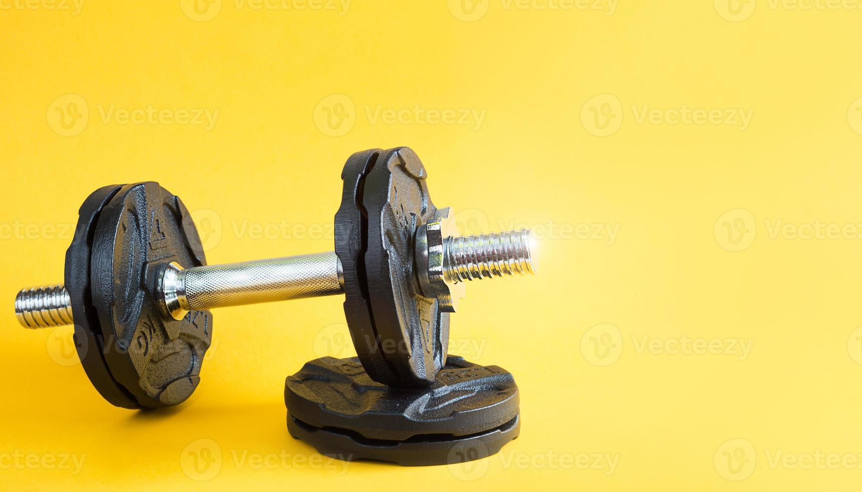 Dumbbell with disks on a yellow background close-up. Sports lifestyle, strength training, gym. Copy space photo