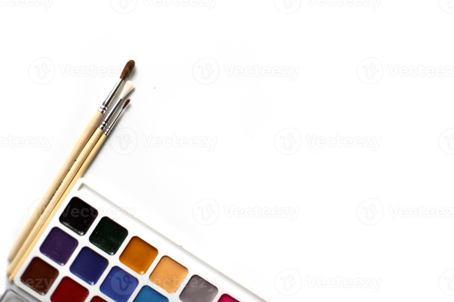 A palette of eighteen-color watercolors and paintbrushes on a white background with space for text. photo