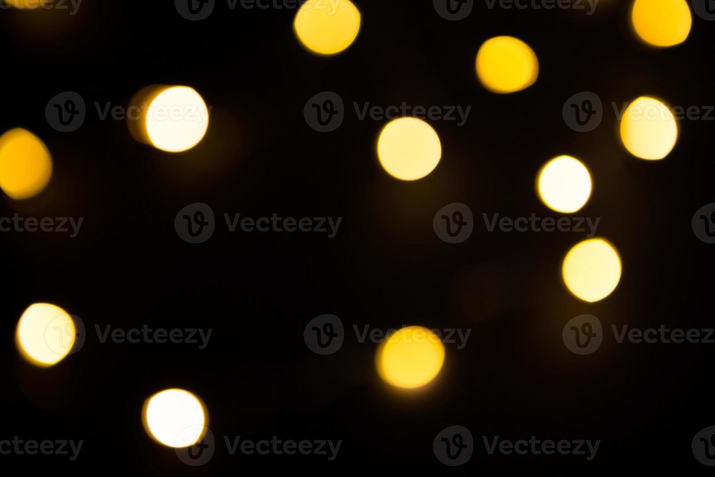 Yellow and gold lights garland in a blur on a black background. Bokeh of flying circles in the defocus. Festive atmosphere of Christmas and new year. Celebrate background photo