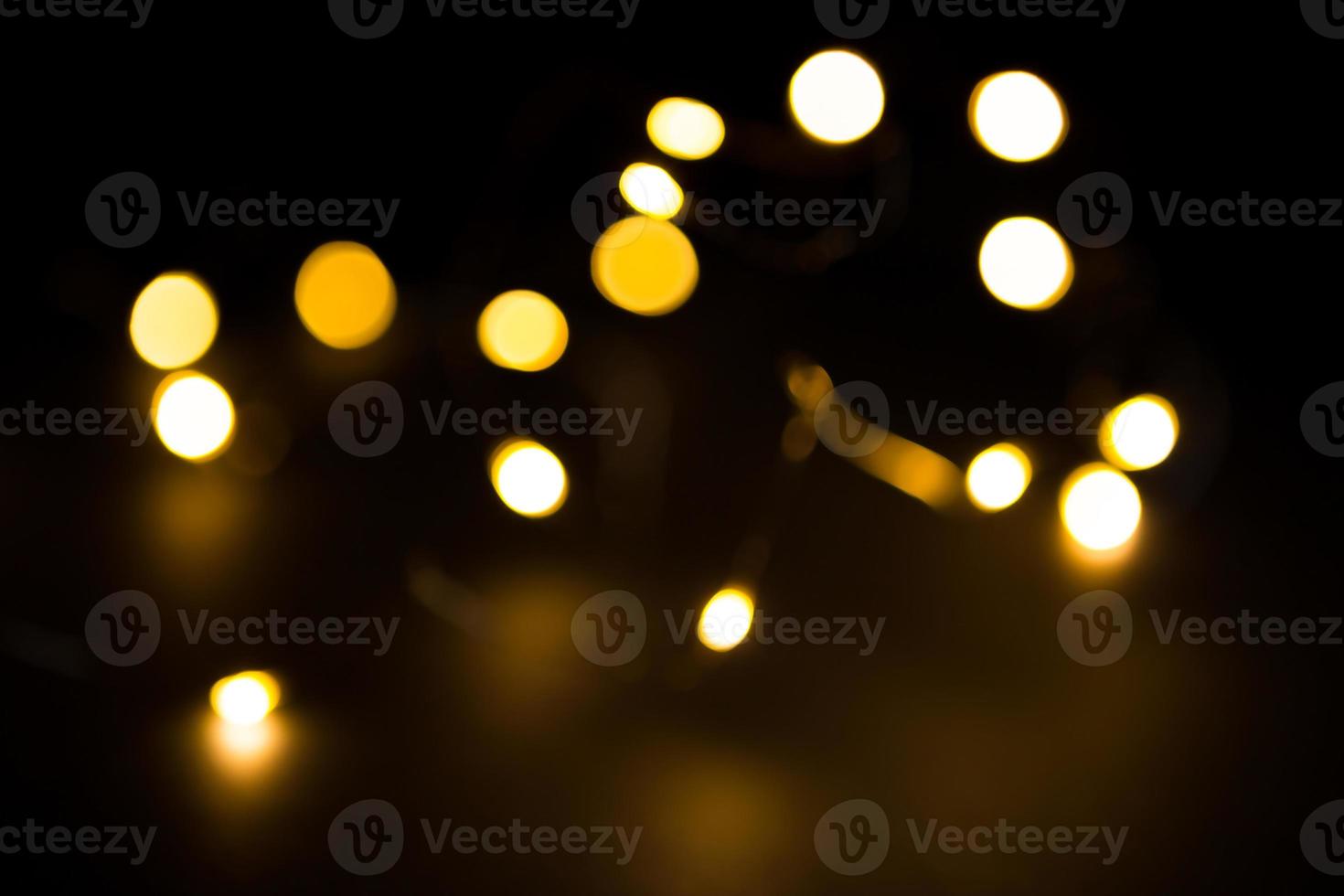 Yellow and gold lights garland in a blur on a black background. Bokeh of flying circles in the defocus. Festive atmosphere of Christmas and new year. Celebrate background photo