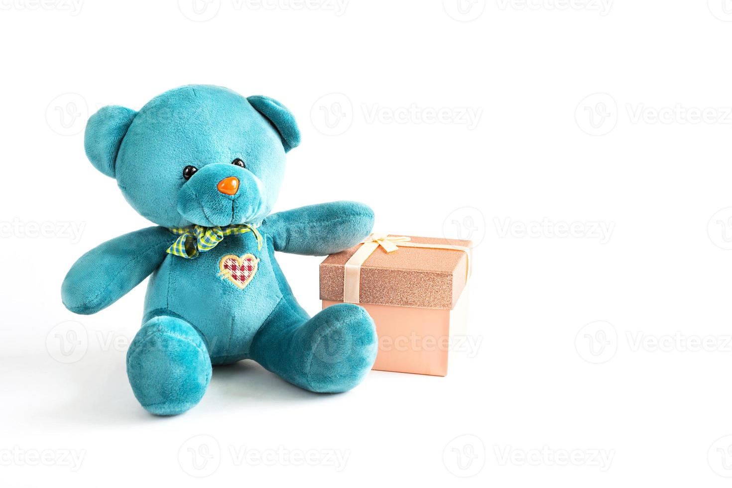 Turquoise soft teddy bear with an embroidered heart holds a gift box and a bow on a white background. Children's toy. Love, a gift to holiday, a declaration of love, Valentine's day. Copy space photo