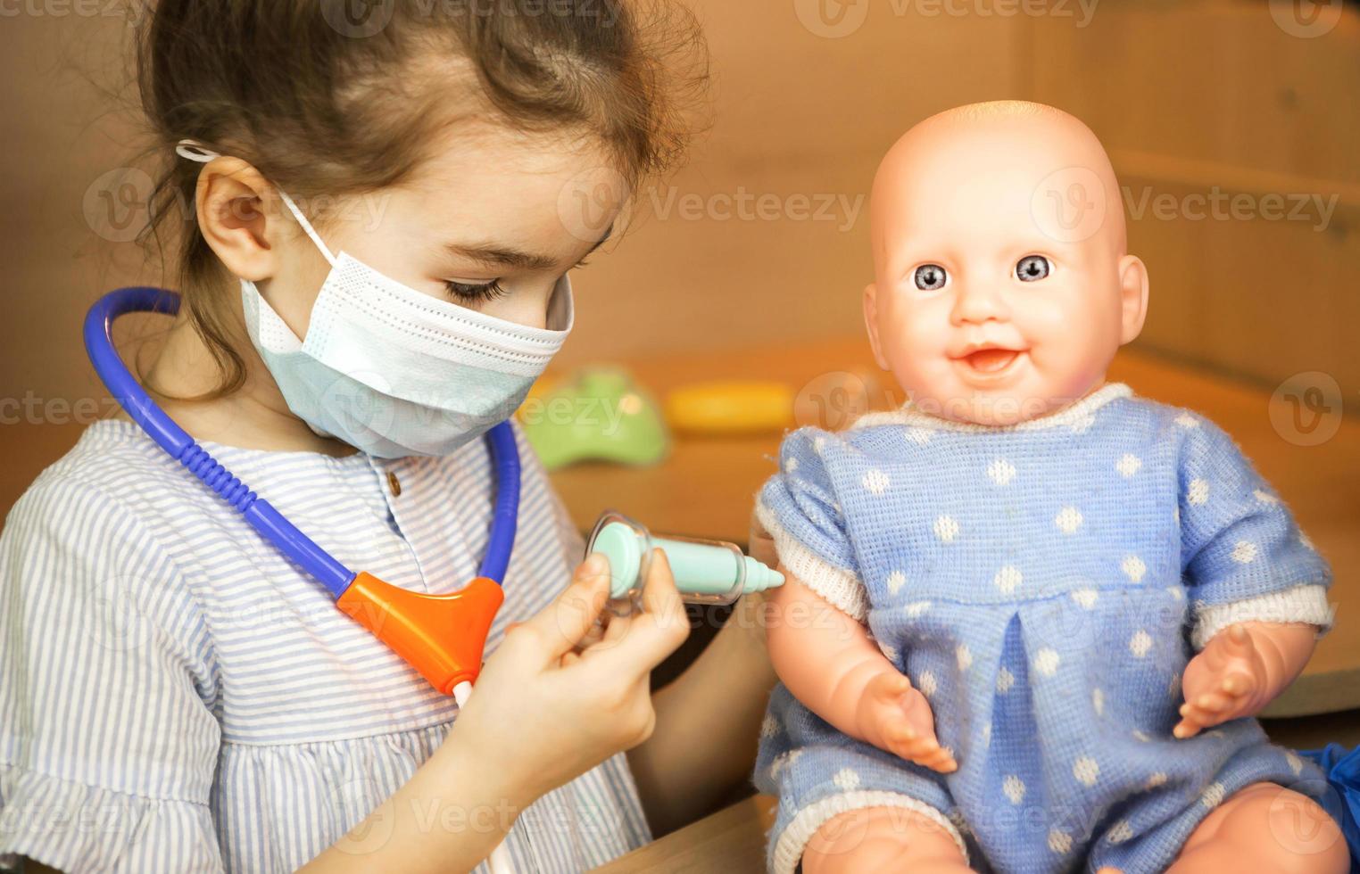 A girl with a doll plays doctor, makes a syringe inoculation in the hand. Vaccination, vaccination calendar, vaccine, profession game. Nurse's injection photo