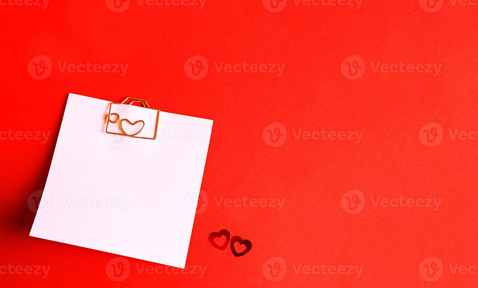 Square sheet for notes with a paper clip in shape of a letter and a heart. Decor of couples in love with hearts on a red background. Valentine's Day, message, greeting, declaration of love. Copy space photo