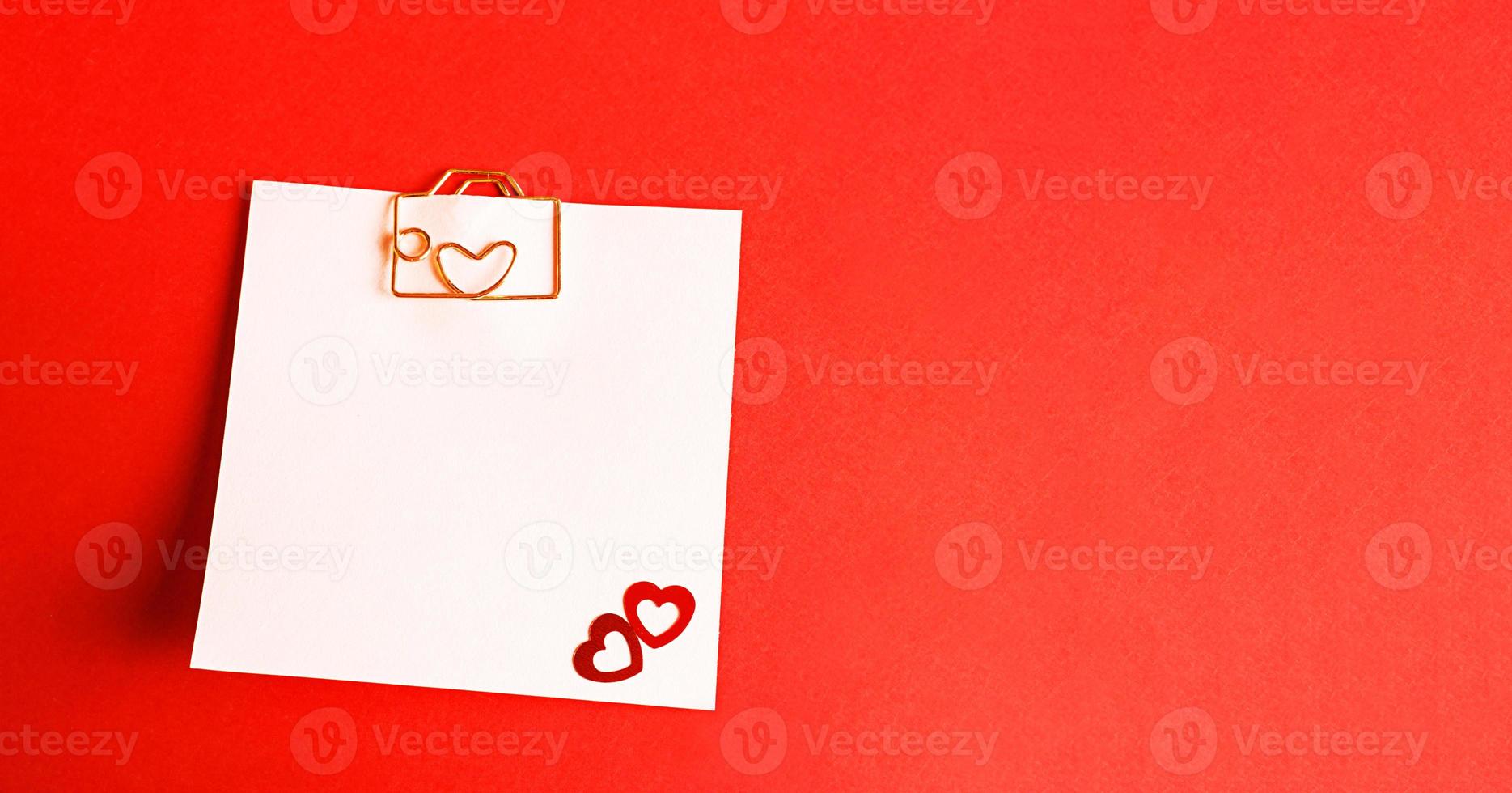 hoja cuadrada para notas con clip en forma de letra y corazón. decoración de parejas enamoradas de corazones sobre un fondo rojo. día de san valentín, mensaje, saludo, declaración de amor. copie el espacio foto