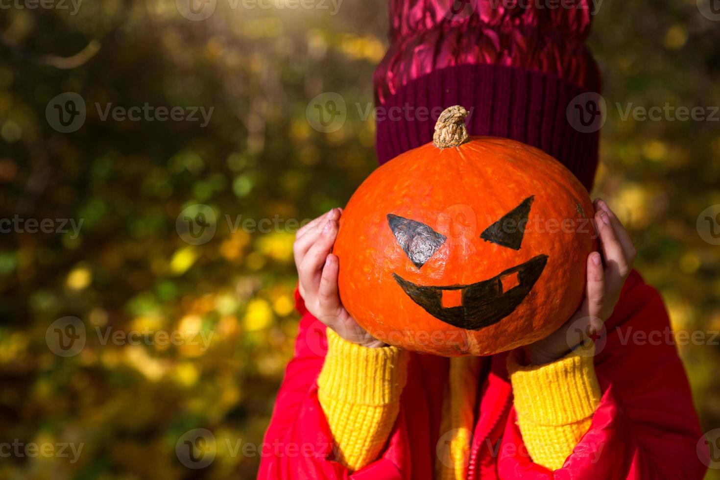 una chica con ropa cálida roja y amarilla sostiene una calabaza con los ojos y la boca pintados en sus manos. halloween, linterna jack, sin rostro. estado de ánimo otoñal, hojas secas amarillas foto