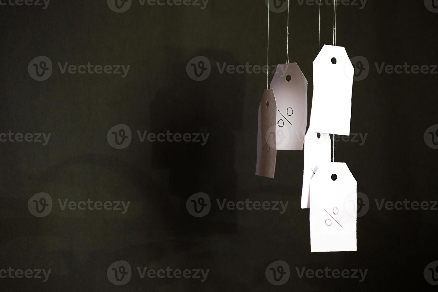 White tags with the percent sign hang on strings on a black background with shadows. Commerce, discount, sale, trade offer. Copy space, mock up. Black Friday photo