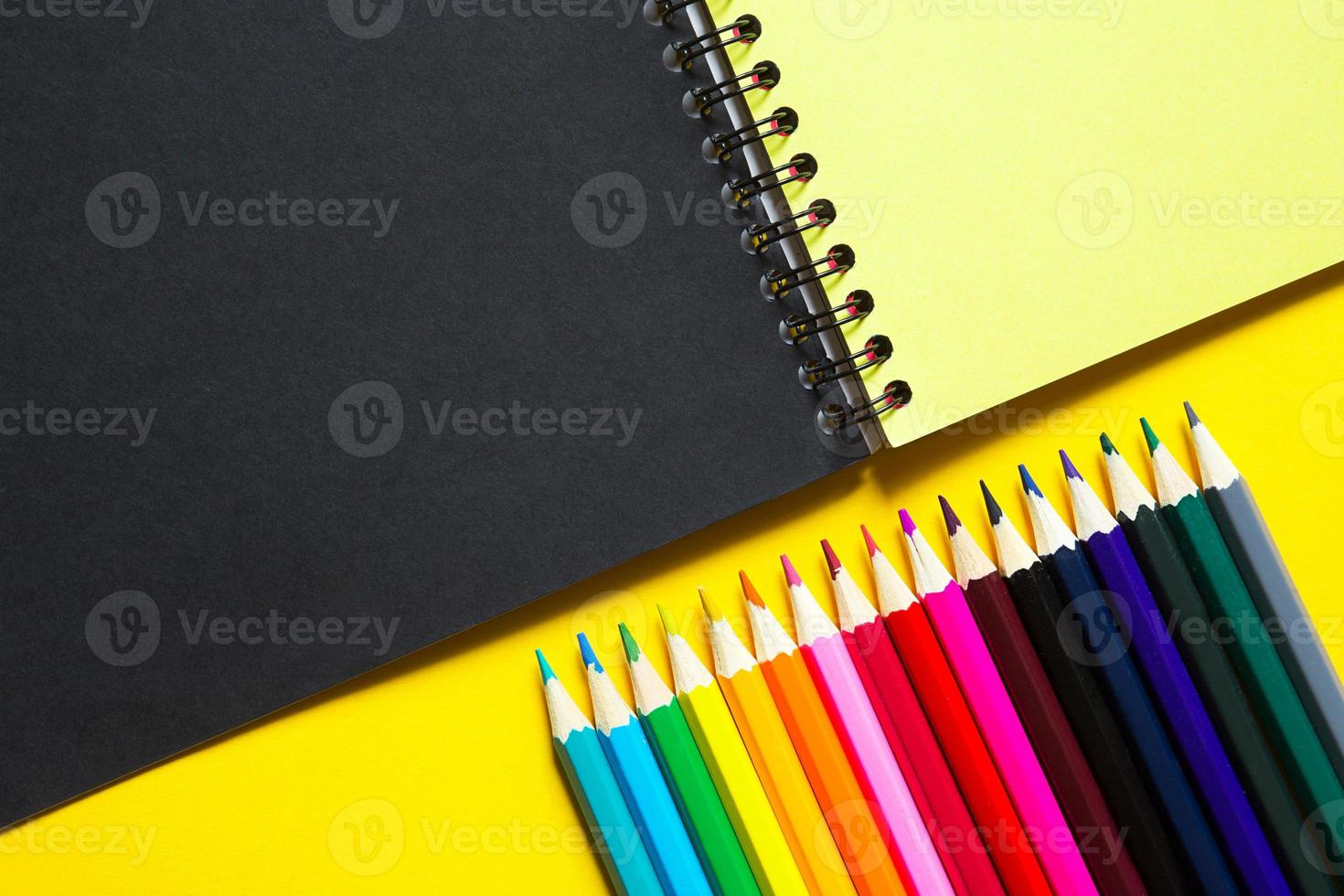 Rainbow palette of colored pencils with a spiral notebook on a yellow background,mock up, flat lay. Back to school, student recruitment, artist, drawing lessons. Copy space. Stationery for creativity photo