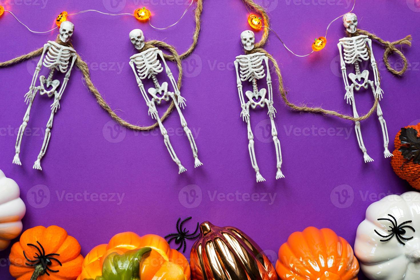 Halloween layout of garland of skeletons on a rope, glowing Jack o Latern, pumpkins, spiders on a purple background. Flat lay horror and a terrible holiday photo