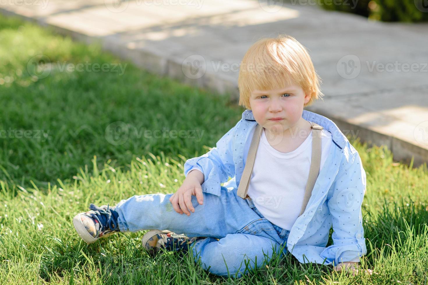 niño rubio se sienta en la hierba verde. foto