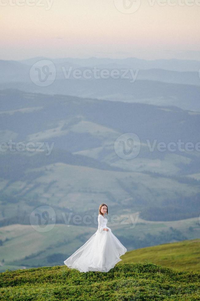 woman in a wedding dress runs across the field toward the mountains photo