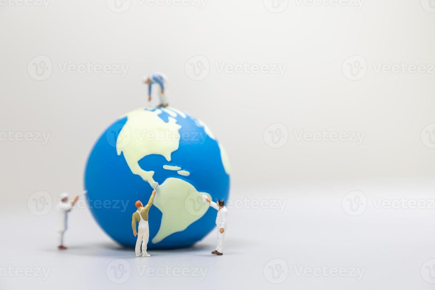 Save Global Environment Care Concept. Close up of group of worker painter miniature people painting and cleaning mini world ball on white table with copy space. photo