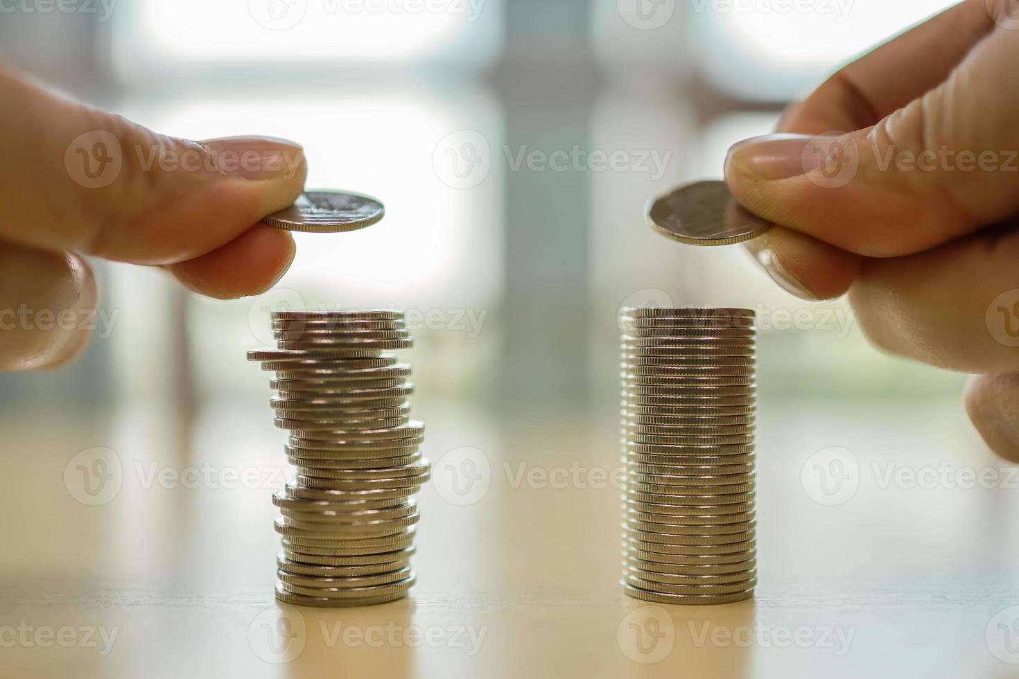 Business, Saving and Retirement concept. Close up of two man hand holding coin and putting down on top of two stack of coins on wooden table. photo