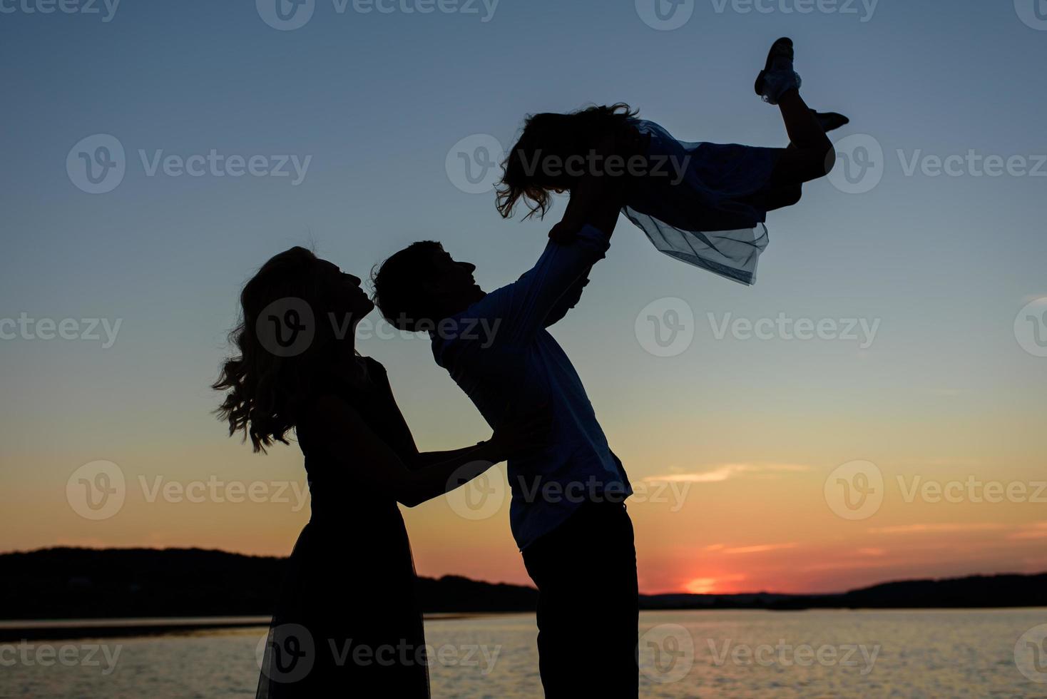 Silhouette of a family of three. Parents throw their daughter into the sky. photo