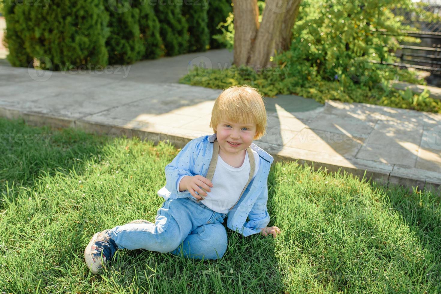 Little blond boy sits on the green grass. photo