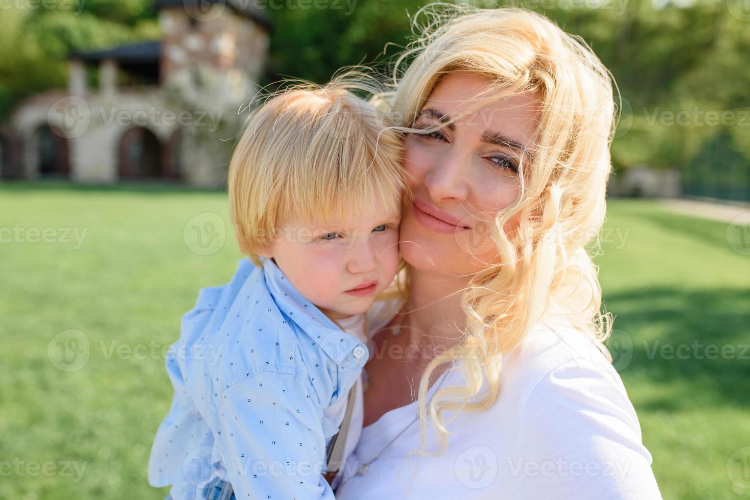 mamá lleva la mano de su hijo a través de la hierba verde. ambas rubias. foto