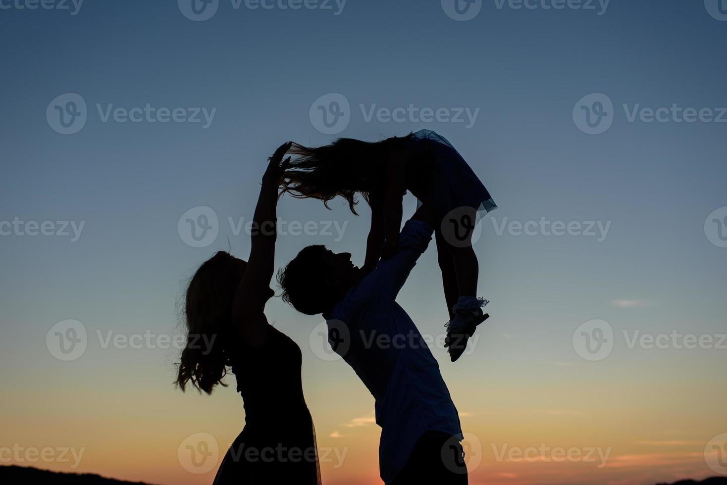 Silhouette of a family of three. Parents throw their daughter into the sky. photo