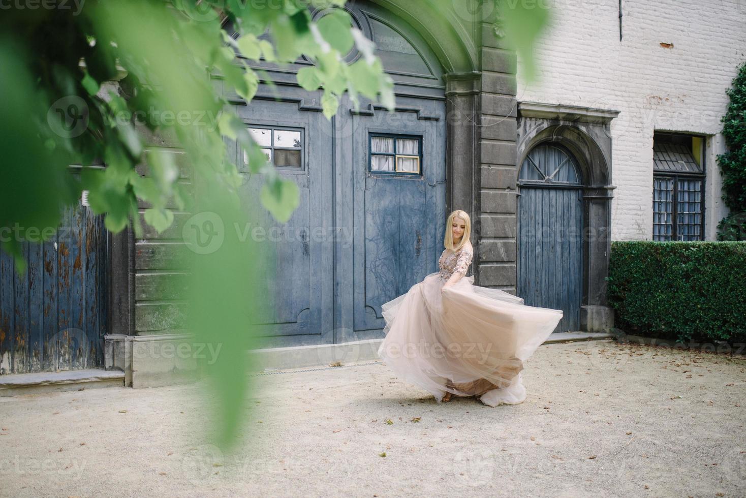 Young beautiful blonde woman in gorgeous blue long dress walking the street near the old building in the old city. photo