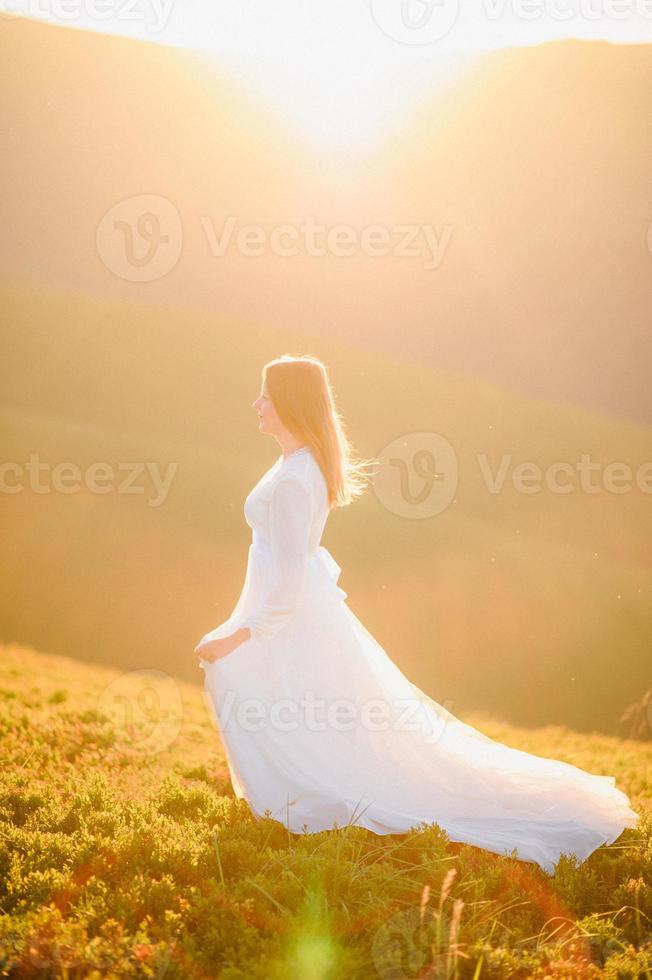 woman in a wedding dress runs across the field toward the mountains photo