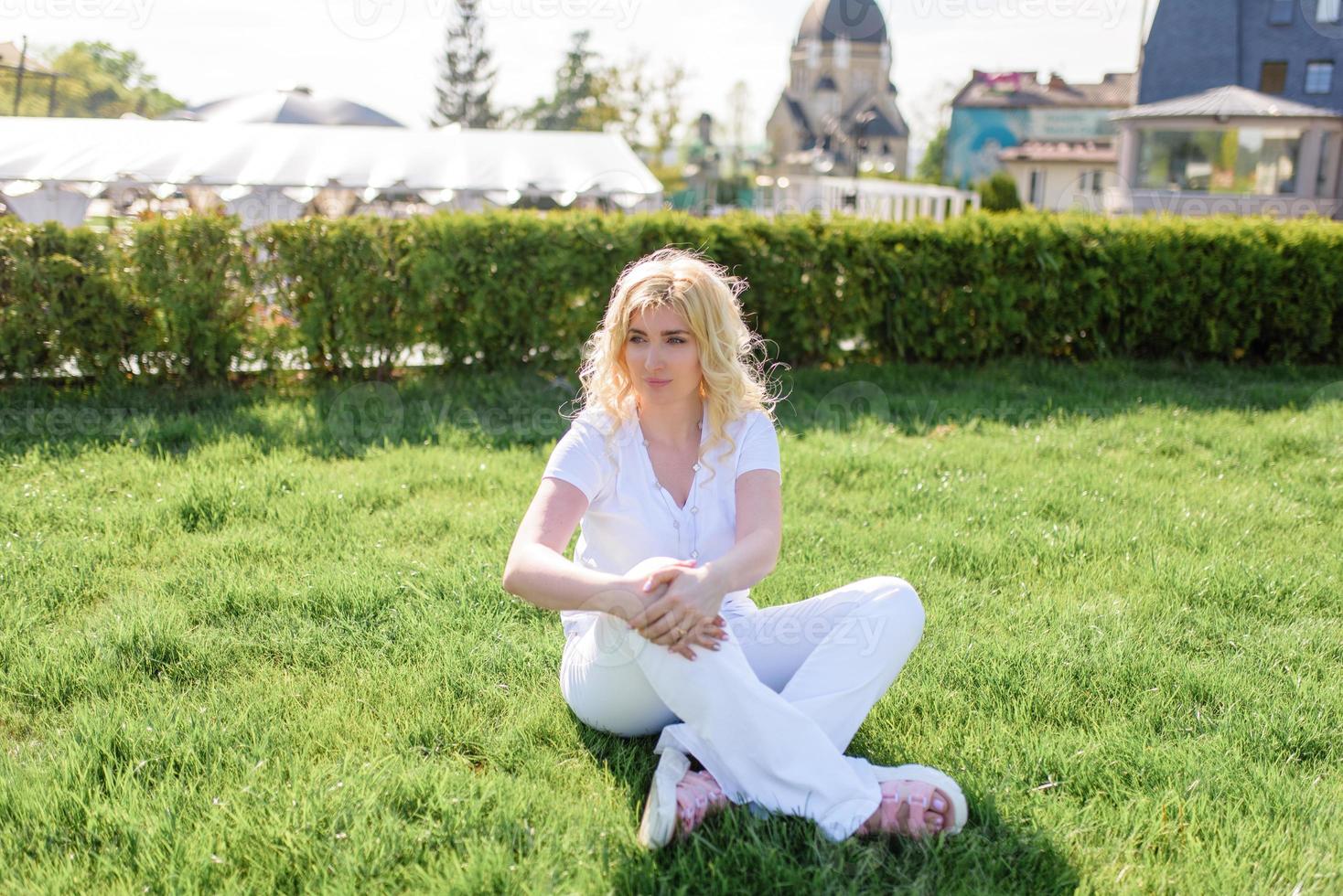 A blond woman is sitting on the grass. photo