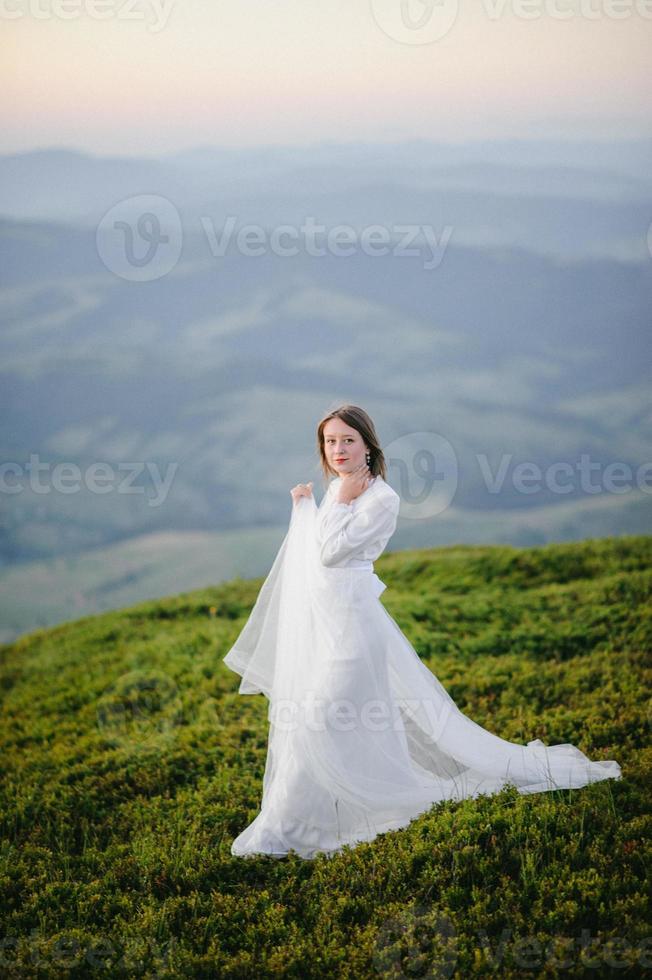 woman in a wedding dress runs across the field toward the mountains photo