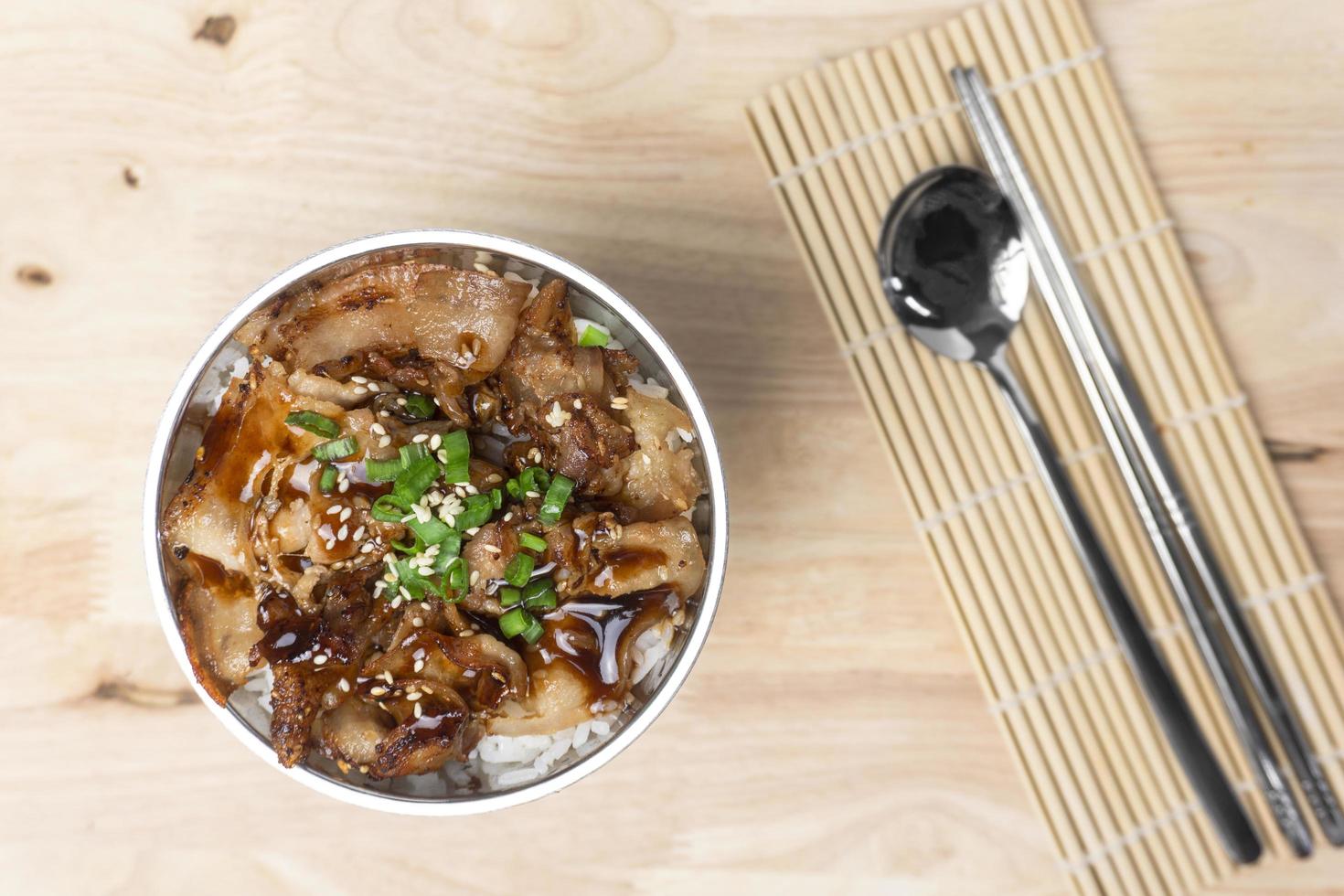 Topview a bowl of rice topped grilled sliced pork belly with soy sauce and sesame seed on the wooden table. photo