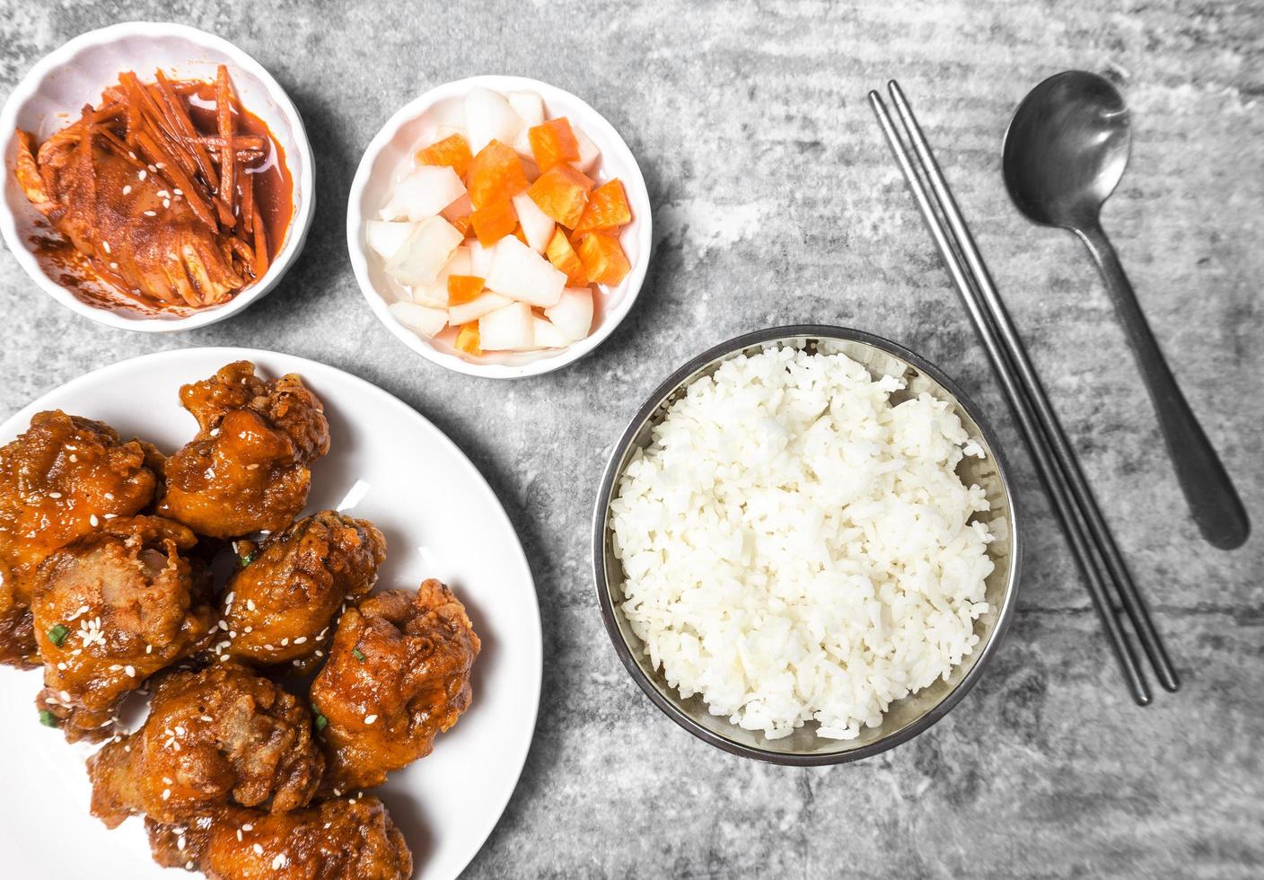 Topview yangnyeom tongdak Korean spicy deep-fried chicken topped white sesame with kimchi and pickled radish side dishes and rice on the gray concrete table, popular street food in Korea. photo