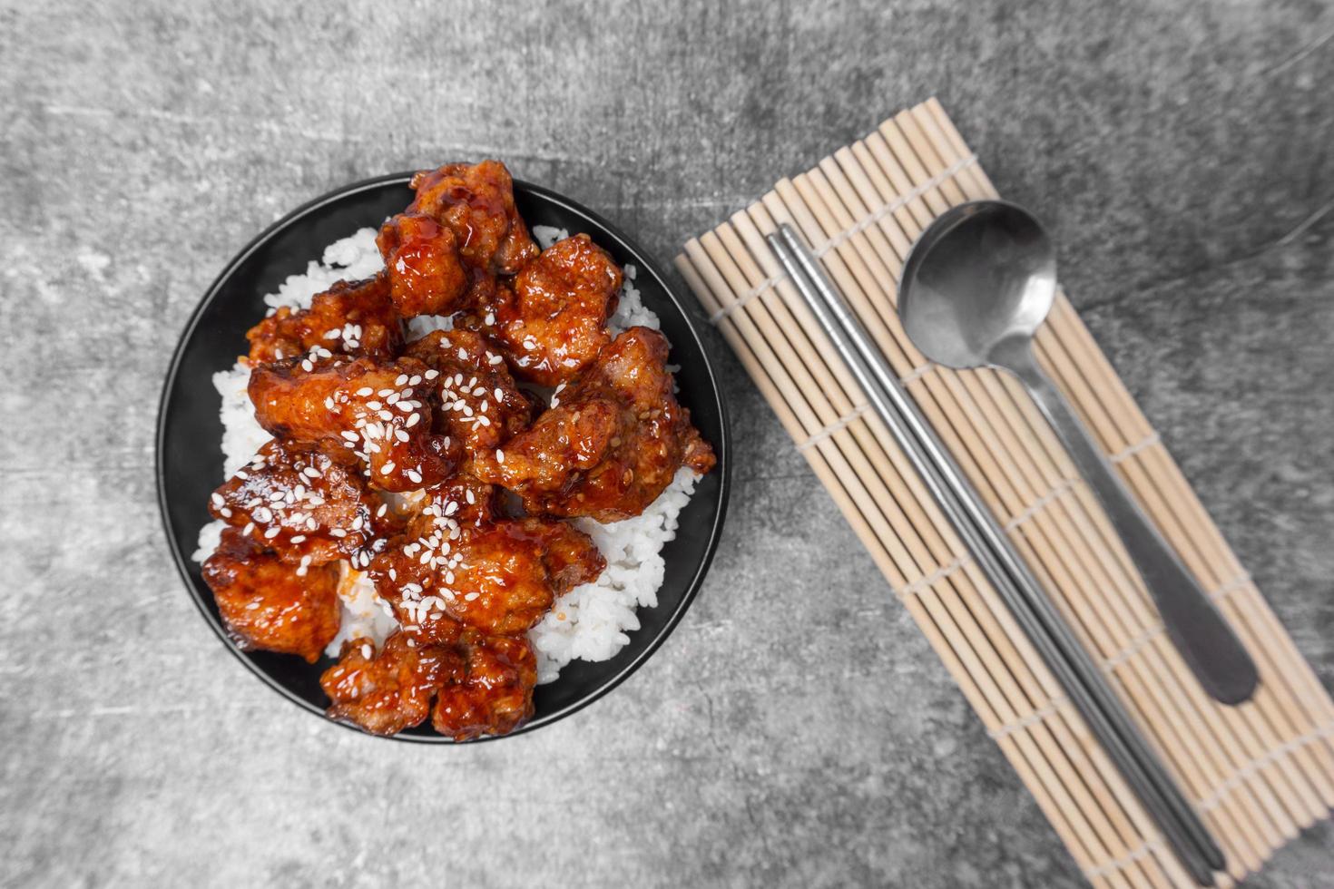 Top view Rice topped Korean spicy deep-fried chicken topped white sesame on the gray concrete table, popular street food in Korea. photo