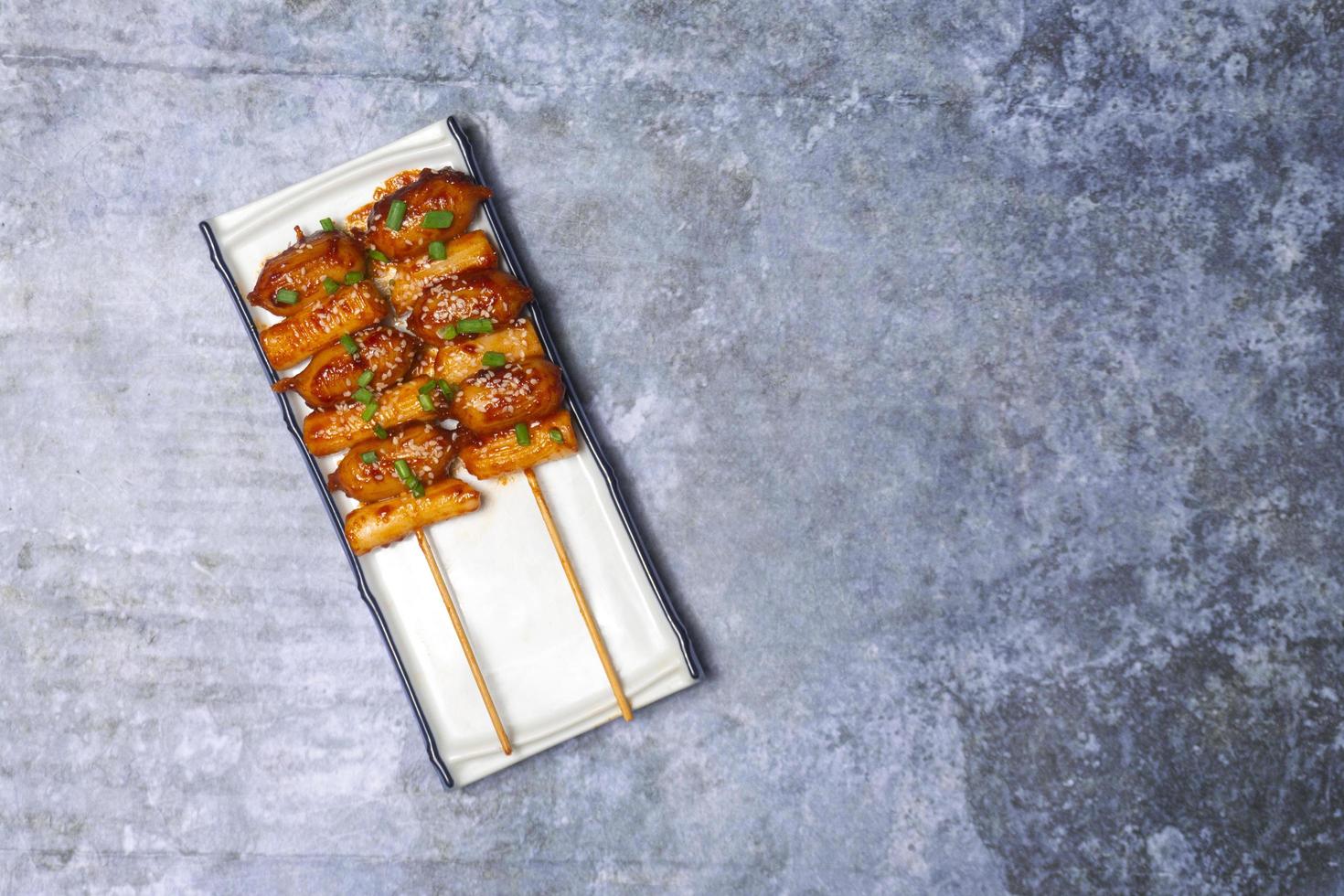 Top view So-tteok is a popular South Korean street food consisting of skewered and rice cake bar and sausage topped with white sesame and green onion leaf. photo