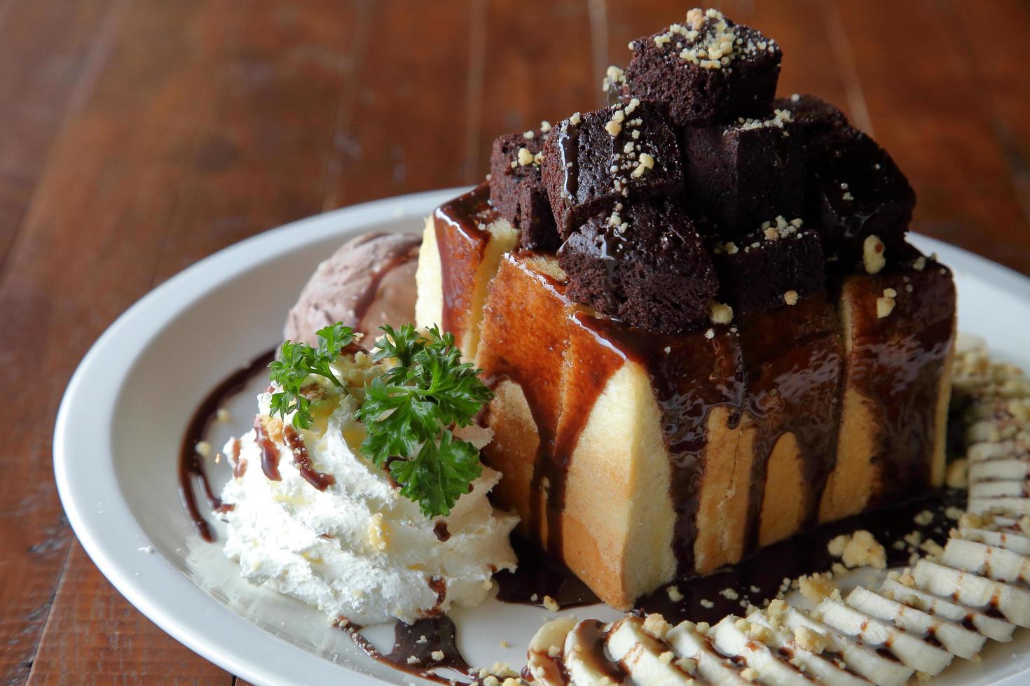 Chocolate honey toast ice cream with mix fruit sliced and whipped cream served on white plate over wooden table photo