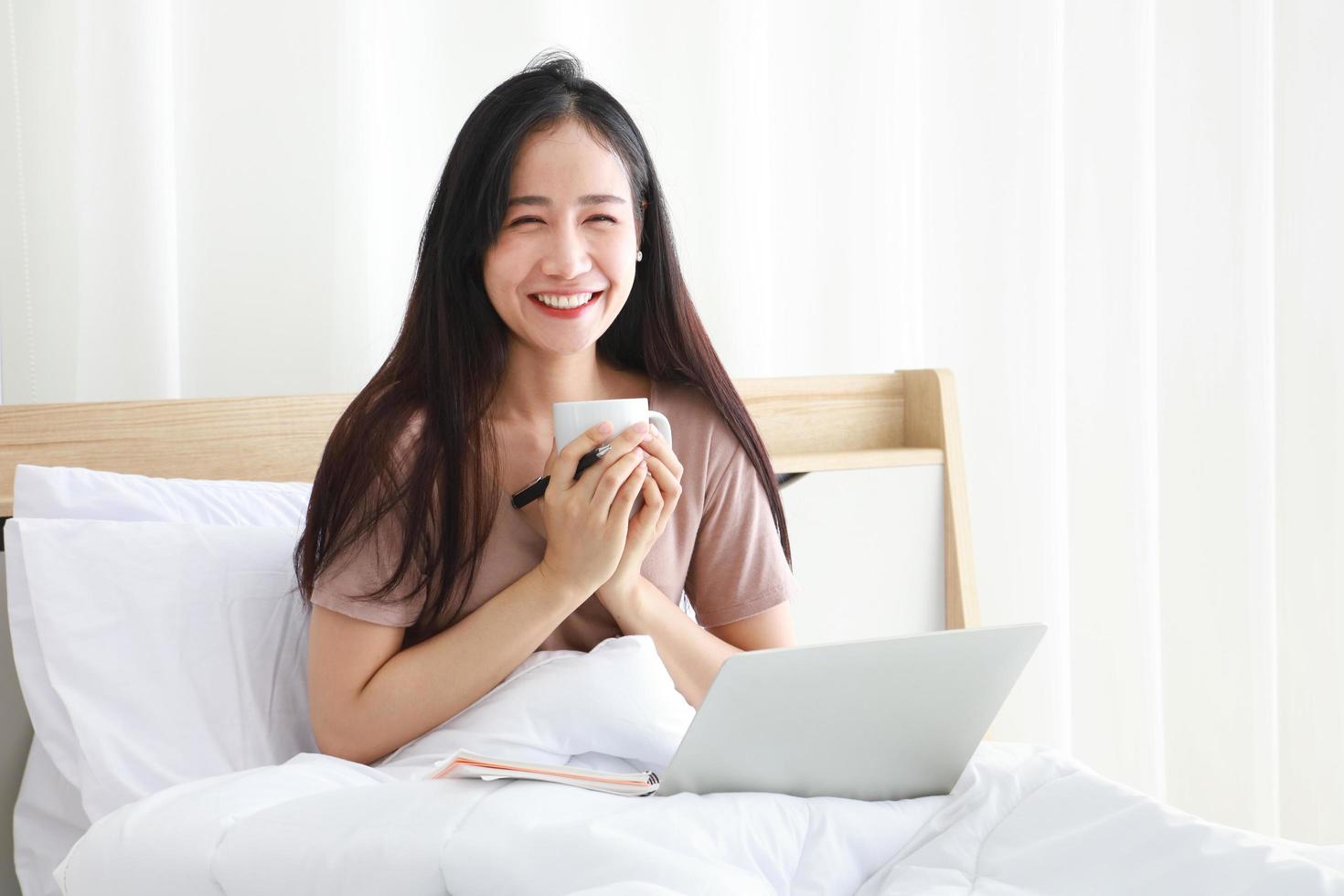 Asian woman working online from home with laptop on her bed for new normal life during quarantine period from covid-19 photo