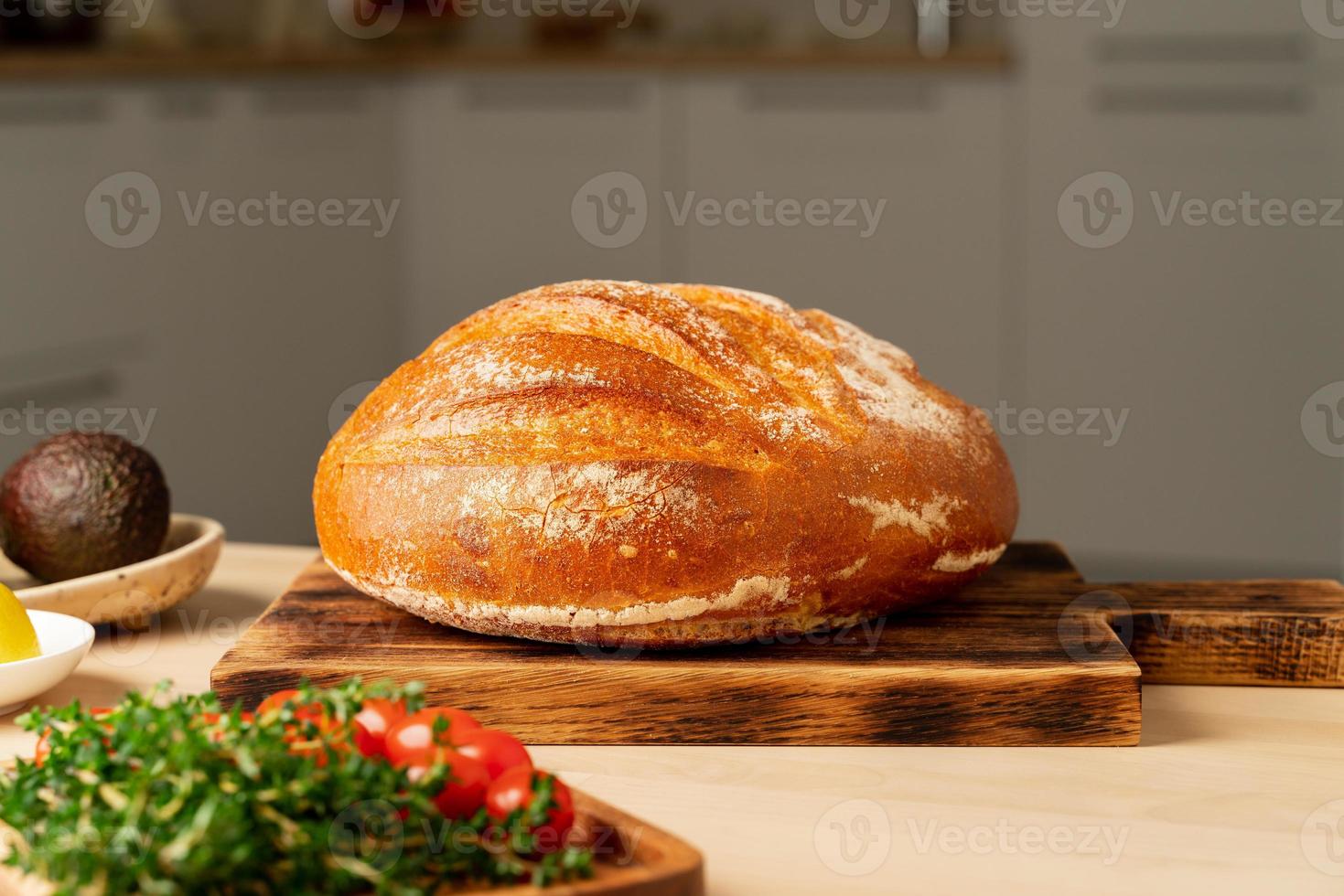 toda la hogaza de pan de trigo blanco recién horneado en una tabla de madera en la mesa de la cocina casera foto