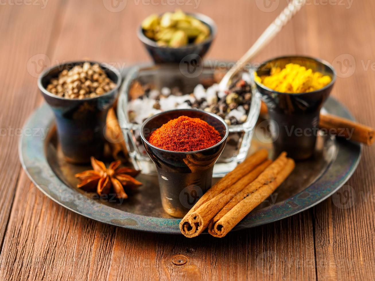 Oriental spice set - coriander, red pepper, turmeric, cinnamon, star anise, rosemary various seasonings in metall cups, on brown wooden table, side view, mcro, selective focus. photo
